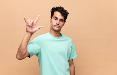 Genç yakışıklı adam kendini mutlu, eğlenceli, kendinden emin, pozitif ve asi hissediyor, elle rock ya da heavy metal işareti yapıyor.