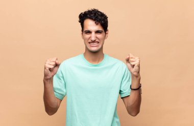 Genç yakışıklı adam mutlu, pozitif ve başarılı hissediyor, zaferi, başarıları ya da iyi şansı kutluyor.