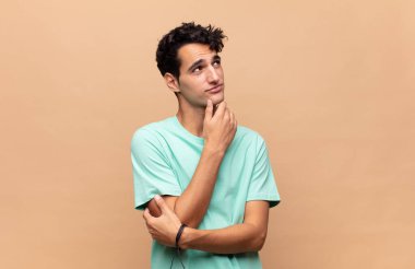 Genç yakışıklı adam düşünceli, meraklı ya da hayal kuruyor, hayal kuruyor ve mekanı kopyalamak için yukarı bakıyor.