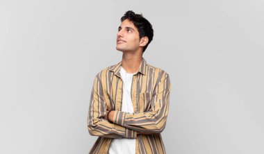 Genç yakışıklı adam mutlu, gururlu ve umutlu, merak ediyor ya da düşünüyor, çapraz kollarla boşluğu dolduruyor.