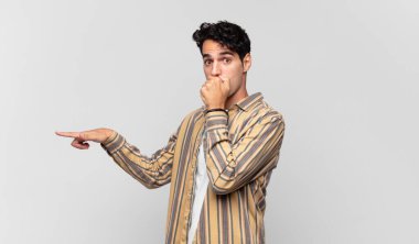 Genç yakışıklı adam kendini mutlu, şaşkın ve şaşırmış hissediyor. Ağzını eliyle kapatıyor ve yanal kopya alanını işaret ediyor.