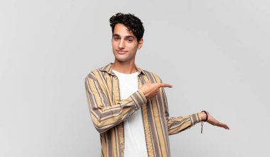 Genç yakışıklı adam gülümsüyor, mutlu, tasasız ve tatmin olmuş hissediyor, fotokopi alanındaki konsepte ya da fikre işaret ediyor.