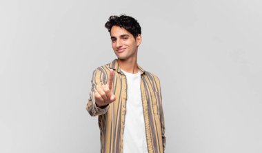 Genç ve yakışıklı bir adam gururla gülümsüyor ve gururla bir numaralı pozu veriyor, kendini lider gibi hissediyor.