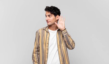 Genç yakışıklı bir adam gülümsüyor, tuhaf bir şekilde yan tarafa bakıyor, dedikoduları dinlemeye ya da bir sırrı duymaya çalışıyor.