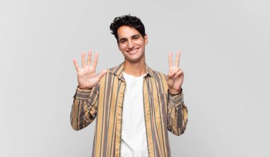 Genç yakışıklı adam gülümsüyor ve dost canlısı görünüyor, 7 ya da 7 numarayı gösteriyor, eli önde, geriye doğru sayıyor.