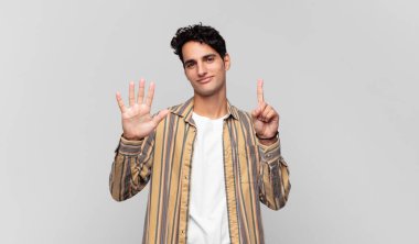 Genç yakışıklı adam gülümsüyor ve arkadaş canlısı görünüyor, altı ya da altıncı numarayı gösteriyor, eli önde, geri sayıyor.