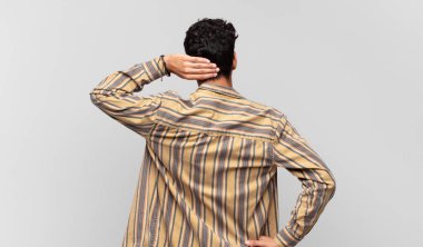 Genç yakışıklı adam düşünüyor ya da şüphe ediyor, kafasını kaşıyor, şaşkın ve kafası karışık hissediyor, arkaya ya da arkaya bakıyor.