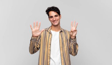 Genç yakışıklı adam gülümsüyor ve arkadaş canlısı görünüyor, 8 ya da 8 numarayı gösteriyor, eli önde, geri sayıyor.