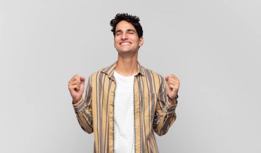 Genç yakışıklı adam çok mutlu ve şaşırmış görünüyor, başarıyı kutluyor, bağırıyor ve zıplıyor.