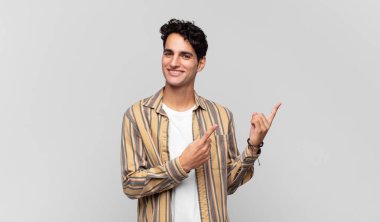 Genç yakışıklı adam mutlu bir şekilde gülümsüyor ve her iki elinde fotokopi alanında nesne gösteriyor.