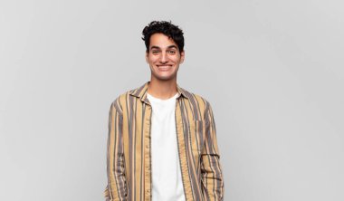 Genç yakışıklı adam mutlu ve şapşal görünüyor. Geniş, eğlenceli, kaçık bir gülüşü ve açık gözleri var.