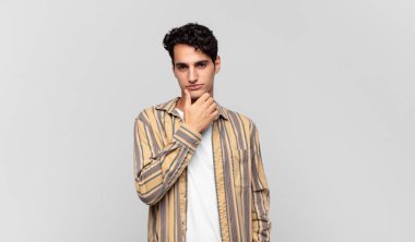 Genç yakışıklı adam ciddi görünüyor, kafası karışık, kararsız ve düşünceli, seçenekler ve seçimler arasında şüpheci.