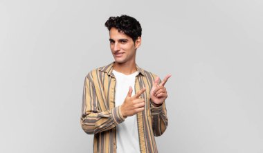 Olumlu, başarılı, mutlu bir tavırla gülümseyen genç yakışıklı adam kamerayı işaret ediyor, elleriyle silah işareti yapıyor.