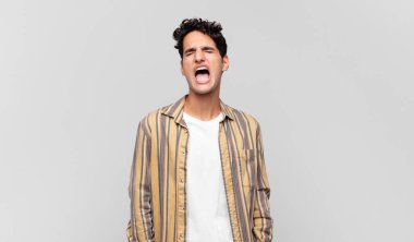 Genç yakışıklı adam öfkeyle bağırıyor, agresif bir şekilde bağırıyor, stresli ve sinirli görünüyor.