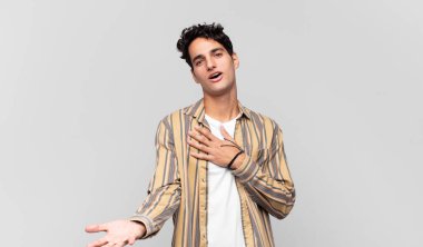 Genç yakışıklı adam mutlu ve aşık, bir eli kalbinin yanında, diğer eli önde uzanmış gülümsüyor.