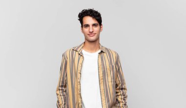 Genç ve yakışıklı bir adam neşeli, neşeli, mutlu, kendinden emin ve rahat bir ifadeyle gülümsüyor.