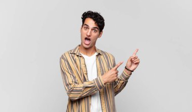 Genç, yakışıklı bir adam kendini neşeli ve şaşırmış hissediyor. Şok olmuş bir ifadeyle gülümsüyor ve bir tarafı işaret ediyor.