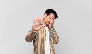 Genç ve yakışıklı bir adam elleriyle yüzünü kapatıyor ve kamerayı durdurmak için diğer elini öne koyuyor. Fotoğraf ya da resimleri reddediyor.