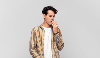 Genç yakışıklı adam tembelce esniyor, uykulu, yorgun ve sıkkın görünüyor.