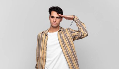 Genç ve yakışıklı bir adam saygı göstererek, onur ve vatanseverlik adına askeri bir selamla kamerayı selamlıyor.