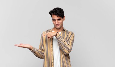 Genç yakışıklı adam neşeyle gülümsüyor ve bir objeyi göstererek veya reklamını yaparak avucundaki fotokopi alanını gösteriyor.