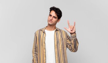 Genç yakışıklı adam kendini mutlu, eğlenceli, kendinden emin, pozitif ve asi hissediyor, elle rock ya da heavy metal işareti yapıyor.