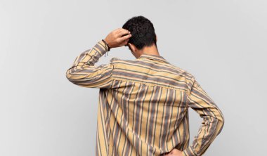 Genç yakışıklı bir adam bilgisiz ve kafası karışık hissediyor, bir çözüm düşünüyor, eli kalçasında, diğeri kafasında, dikiz aynasından.