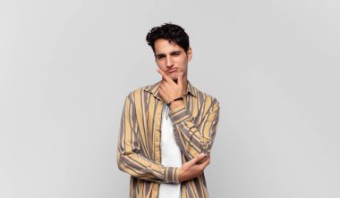 Genç yakışıklı adam ciddi, düşünceli ve güvensiz görünüyor, bir kolu çapraz ve çene üzerinde, seçenekleri tartıyor