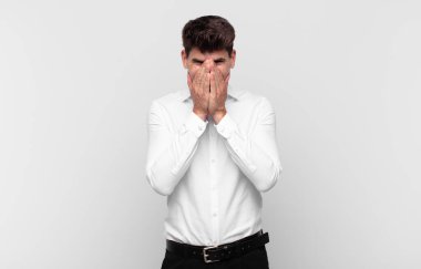 Genç yakışıklı adam mutlu, neşeli, şanslı ve şaşkın görünüyor. İki eliyle ağzını kapatıyor.