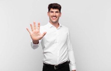 Genç yakışıklı adam gülümsüyor ve arkadaş canlısı görünüyor, 5 ya da 5 numarayı gösteriyor, eli önde, geriye doğru sayıyor.