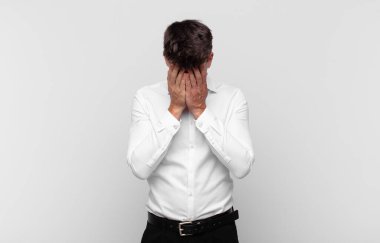 Genç yakışıklı adam üzgün, hayal kırıklığına uğramış, gergin ve depresif, iki eliyle yüzünü kaplayan, ağlayan