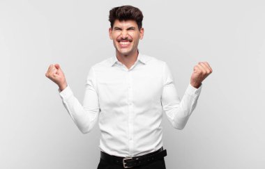 Genç yakışıklı adam çok mutlu ve şaşırmış görünüyor, başarıyı kutluyor, bağırıyor ve zıplıyor.