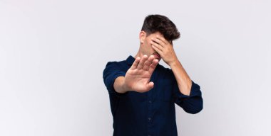 Genç ve yakışıklı bir adam elleriyle yüzünü kapatıyor ve kamerayı durdurmak için diğer elini öne koyuyor. Fotoğraf ya da resimleri reddediyor.