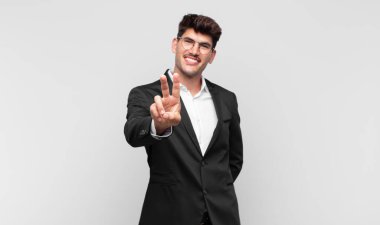 Genç yakışıklı adam gülümsüyor ve mutlu görünüyor, kaygısız ve olumlu, zafer veya barış işareti yapıyor.