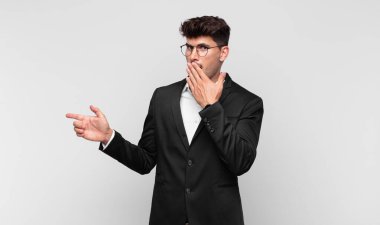 Genç yakışıklı adam kendini mutlu, şaşkın ve şaşırmış hissediyor. Ağzını eliyle kapatıyor ve yanal kopya alanını işaret ediyor.