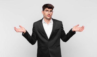 Genç yakışıklı adam şaşkın ve şaşkın, şüpheci, farklı seçenekleri tartıyor ya da komik bir ifadeyle seçiyor.