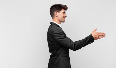 Genç yakışıklı adam gülümsüyor, seni selamlıyor ve başarılı bir anlaşma için el sıkışmayı teklif ediyor.