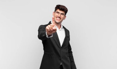 Genç ve yakışıklı bir adam gururla gülümsüyor ve gururla bir numaralı pozu veriyor, kendini lider gibi hissediyor.