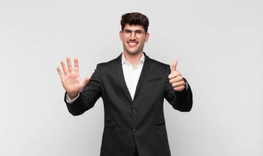 Genç yakışıklı adam gülümsüyor ve arkadaş canlısı görünüyor, altı ya da altıncı numarayı gösteriyor, eli önde, geri sayıyor.