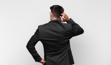 Genç yakışıklı adam düşünüyor ya da şüphe ediyor, kafasını kaşıyor, şaşkın ve kafası karışık hissediyor, arkaya ya da arkaya bakıyor.