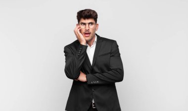 Genç yakışıklı adam şok ve inançsızlık içinde, elleri yanak ve kolları çapraz, sersemlemiş ve şaşırmış hissediyor.