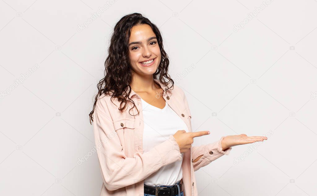 pretty young woman smiling, feeling happy, carefree and satisfied, pointing to concept or idea on copy space on the side