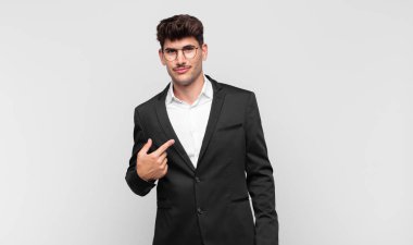 Genç yakışıklı, gururlu, kendinden emin ve mutlu görünüyor, gülümsüyor ve kendini işaret ediyor ya da bir numara işareti yapıyor.