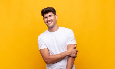 Genç yakışıklı adam utangaç ve neşeli bir şekilde gülüyor, arkadaş canlısı ve olumlu ama güvensiz bir tavırla.