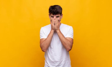 Genç yakışıklı adam mutlu, neşeli, şanslı ve şaşkın görünüyor. İki eliyle ağzını kapatıyor.