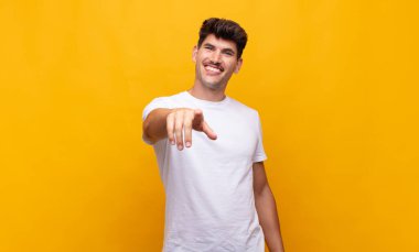 Genç ve yakışıklı bir adam kameraya bakıyor. Tatmin olmuş, kendine güvenen, dost canlısı bir gülümsemeyle seni seçiyor.