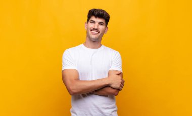 Genç yakışıklı adam mutlu, gururlu ve umutlu, merak ediyor ya da düşünüyor, çapraz kollarla boşluğu dolduruyor.