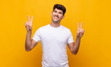 Genç yakışıklı adam gülümsüyor ve mutlu görünüyor, arkadaş canlısı ve memnun, işaret eden zafer ya da barış iki elle