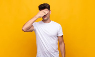 Genç yakışıklı bir adam tek eliyle gözlerini kapatıyor. Korkmuş ya da endişeli, merak ediyor ya da körü körüne bir sürpriz bekliyor.