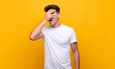 Genç yakışıklı adam şok olmuş, korkmuş ya da korkmuş görünüyor. Yüzü elle kaplanmış ve parmaklarının arasından gizlice bakıyor.